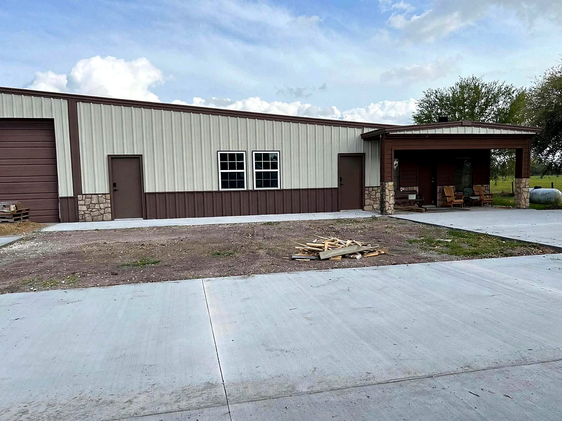 Completed steel building with metal siding, stone base and covered porch in rural Texas