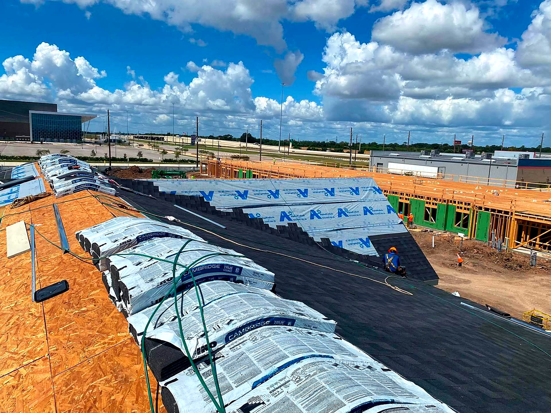 Crew installing architectural shingles over synthetic underlayment on a new retail building