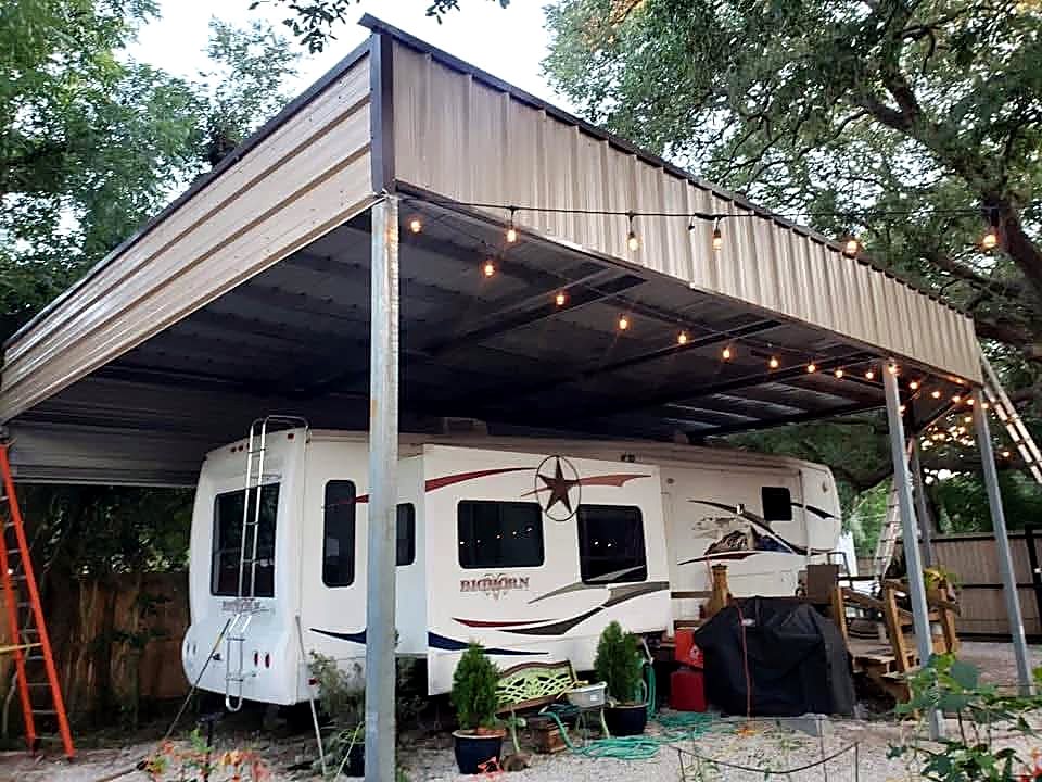 Tall steel RV cover with string lights over a fifth wheel under oak trees
