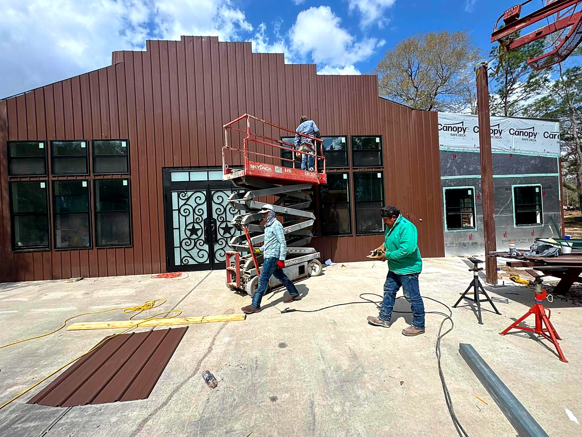 Crew installing brown metal wall panels on a stepped-parapet building facade
