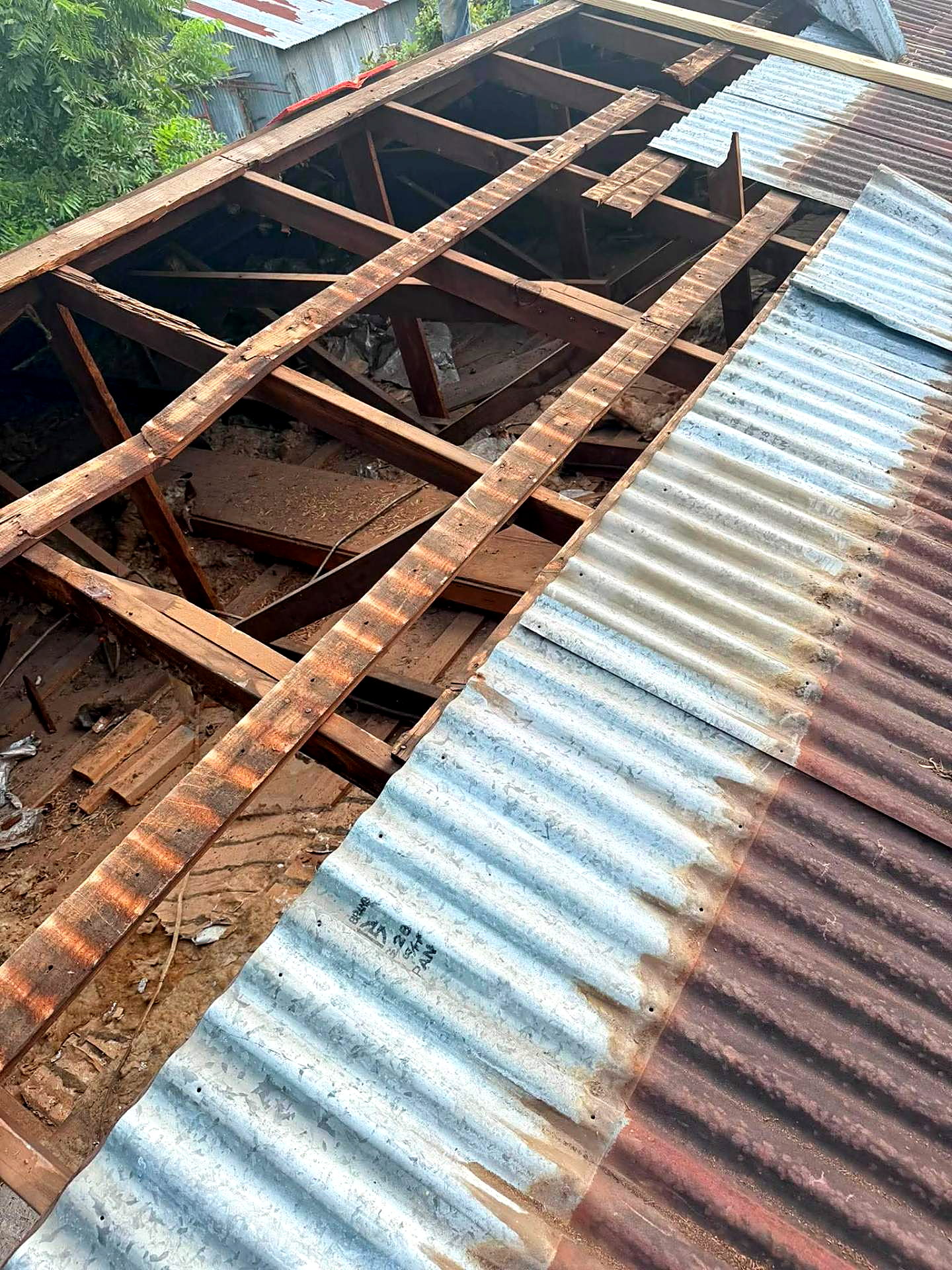 Rusted corrugated metal panels removed to expose deteriorated purlins