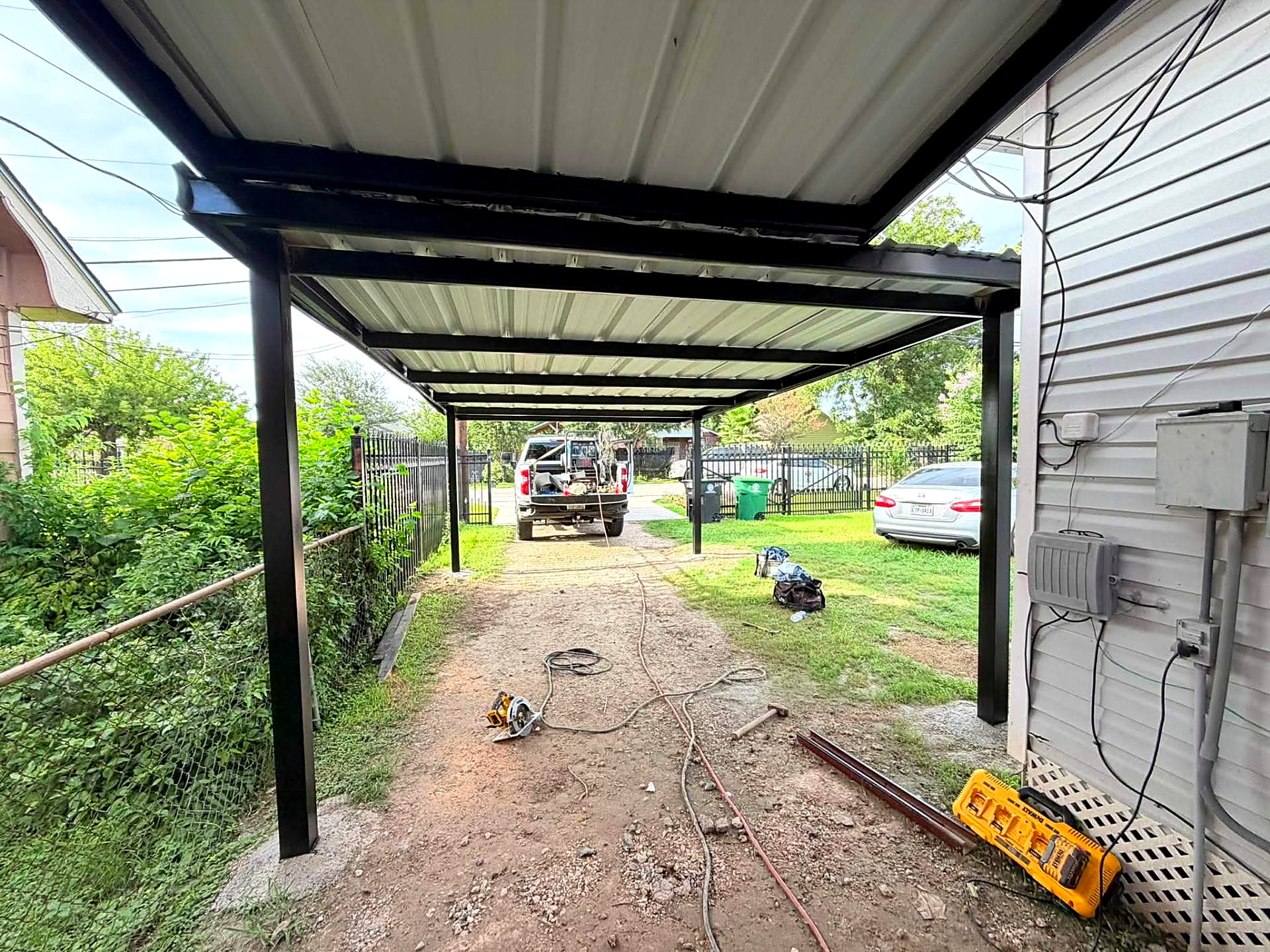 Attached steel carport with welded black frame and white metal roof panels at a Houston home