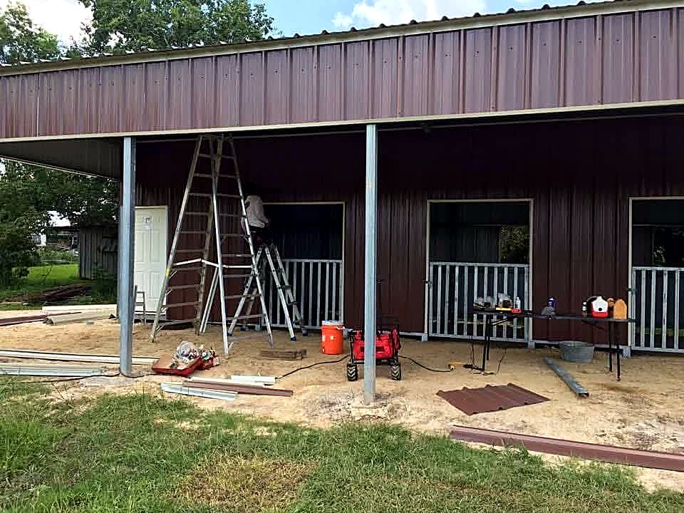 Crew fitting trim and door framing on a brown metal barn stall run