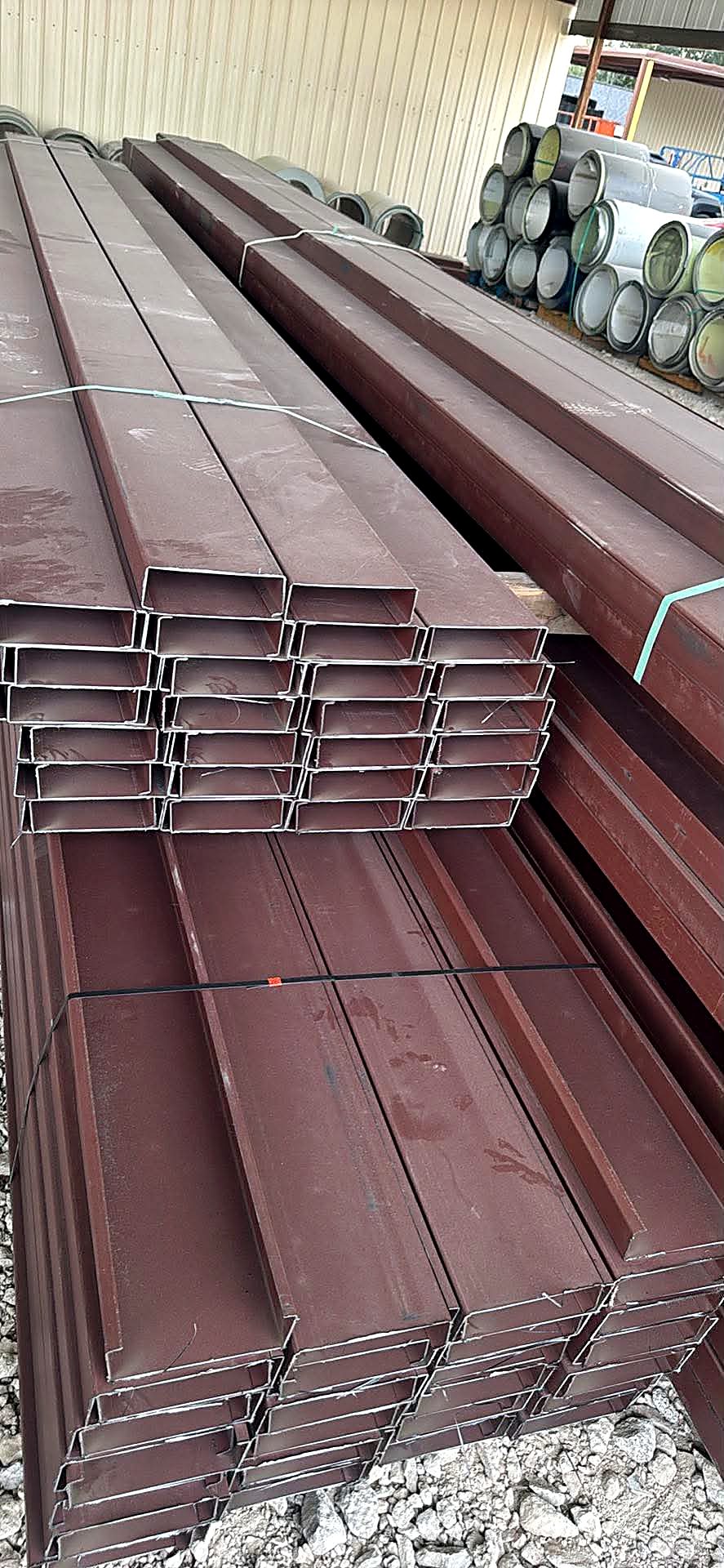 Bundles of primer-coated steel C-purlins and beams stacked at the yard