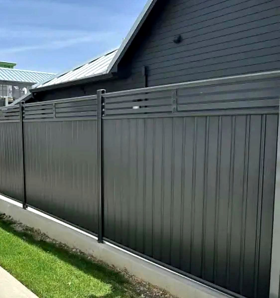 Grey metal fence with a horizontal slat top section on a concrete kerb