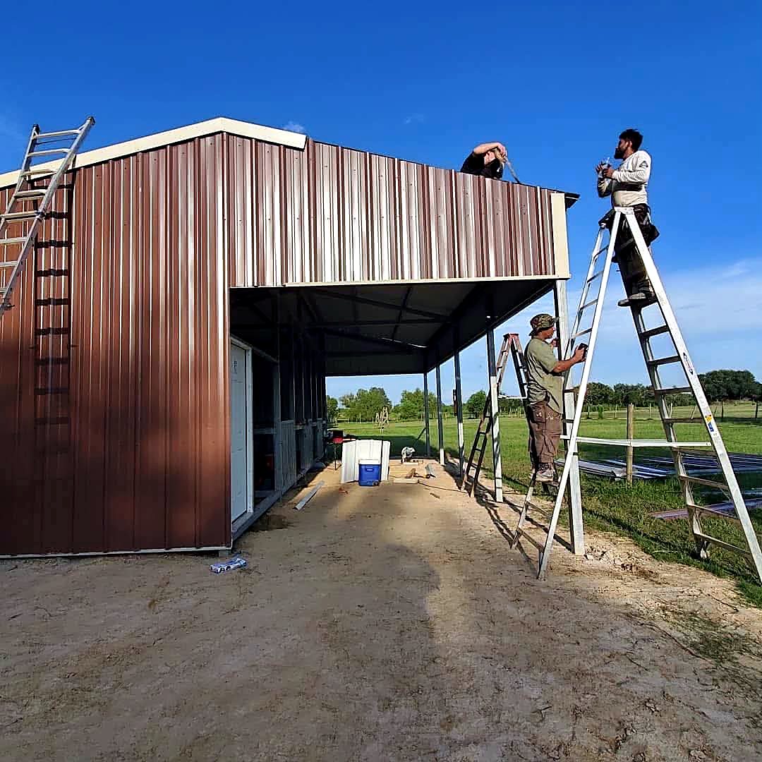 Crew on ladders fixing brown wall panels to a new steel barn frame