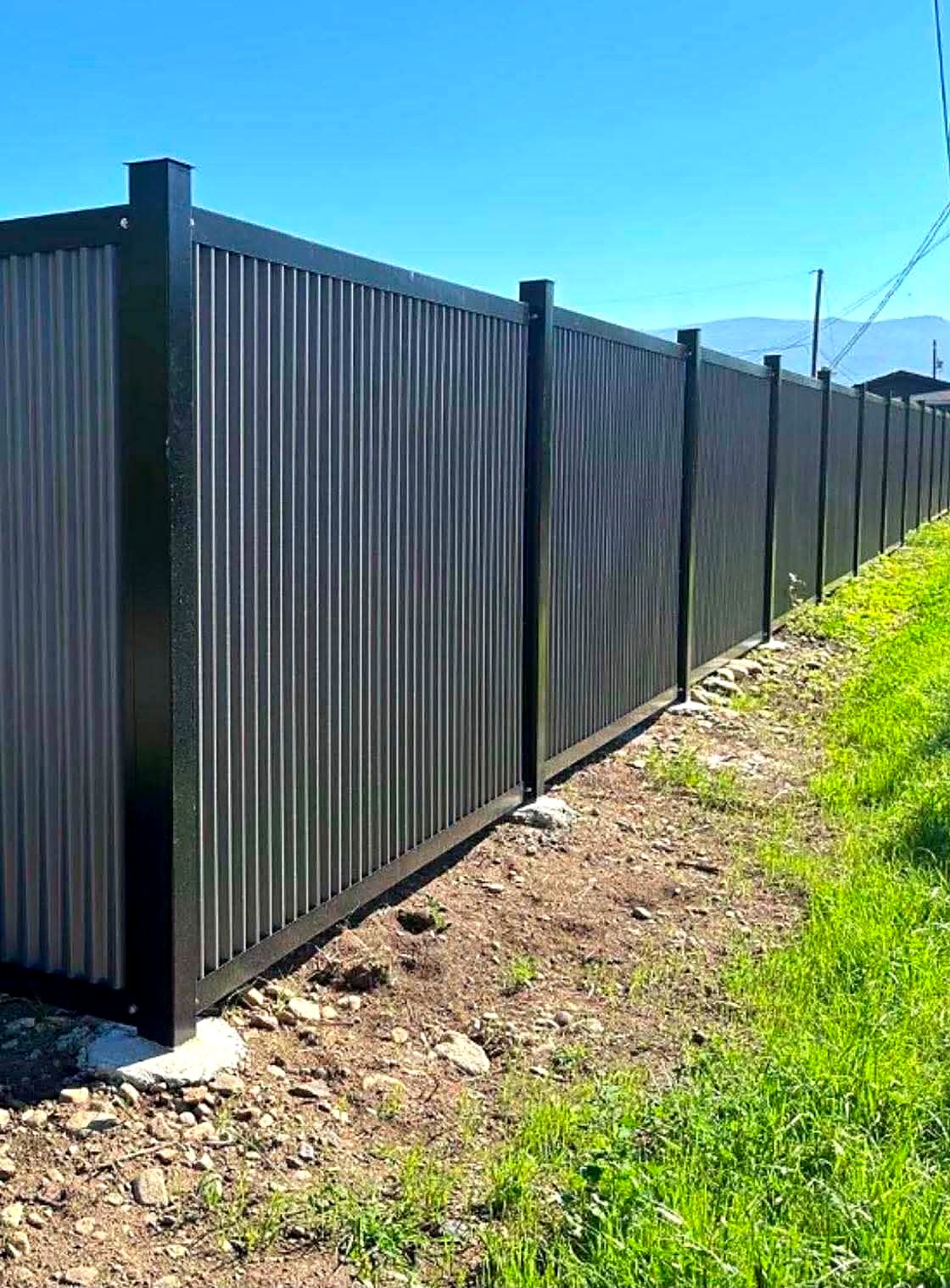 Long run of black corrugated metal privacy fencing on steel posts
