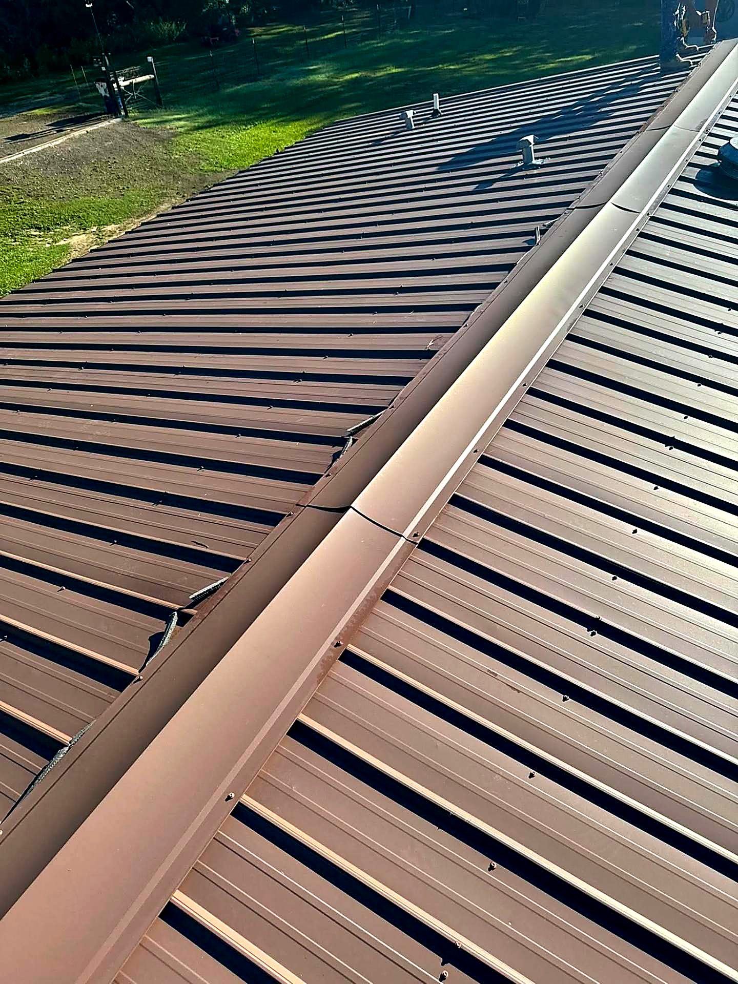 Brown standing seam metal roof with formed ridge cap in sunlight
