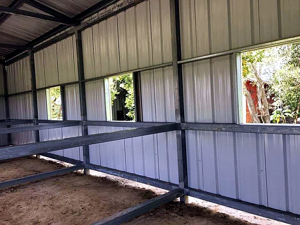 Interior of a steel barn showing wall sheeting, window openings and stall rails