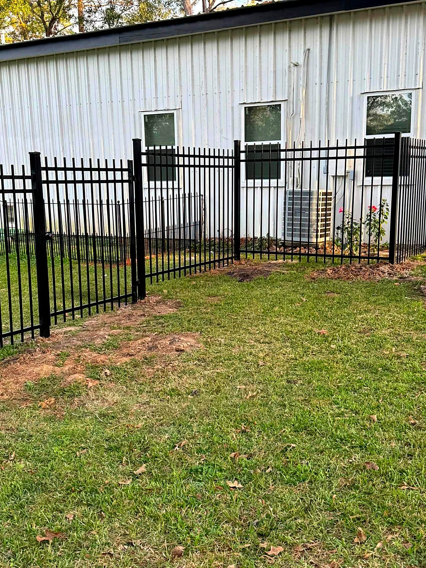 Black iron fence and gate running around a white metal shop building