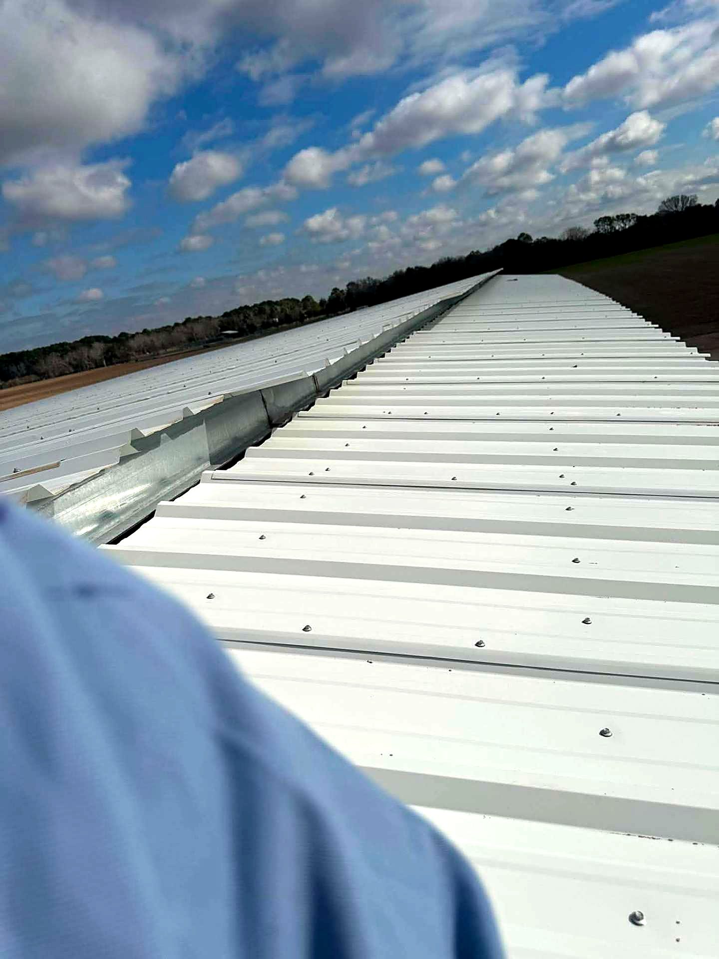 Long run of white ribbed metal roofing along a ridge line under a Texas sky
