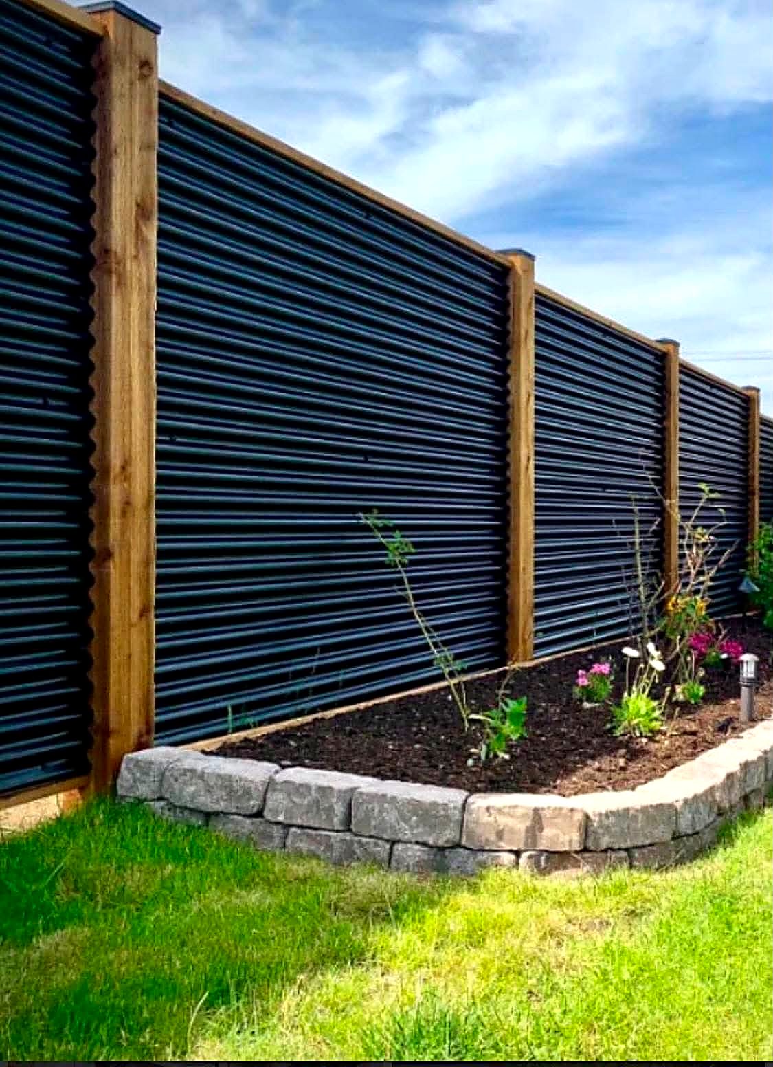 Black corrugated metal fence panels framed between timber posts