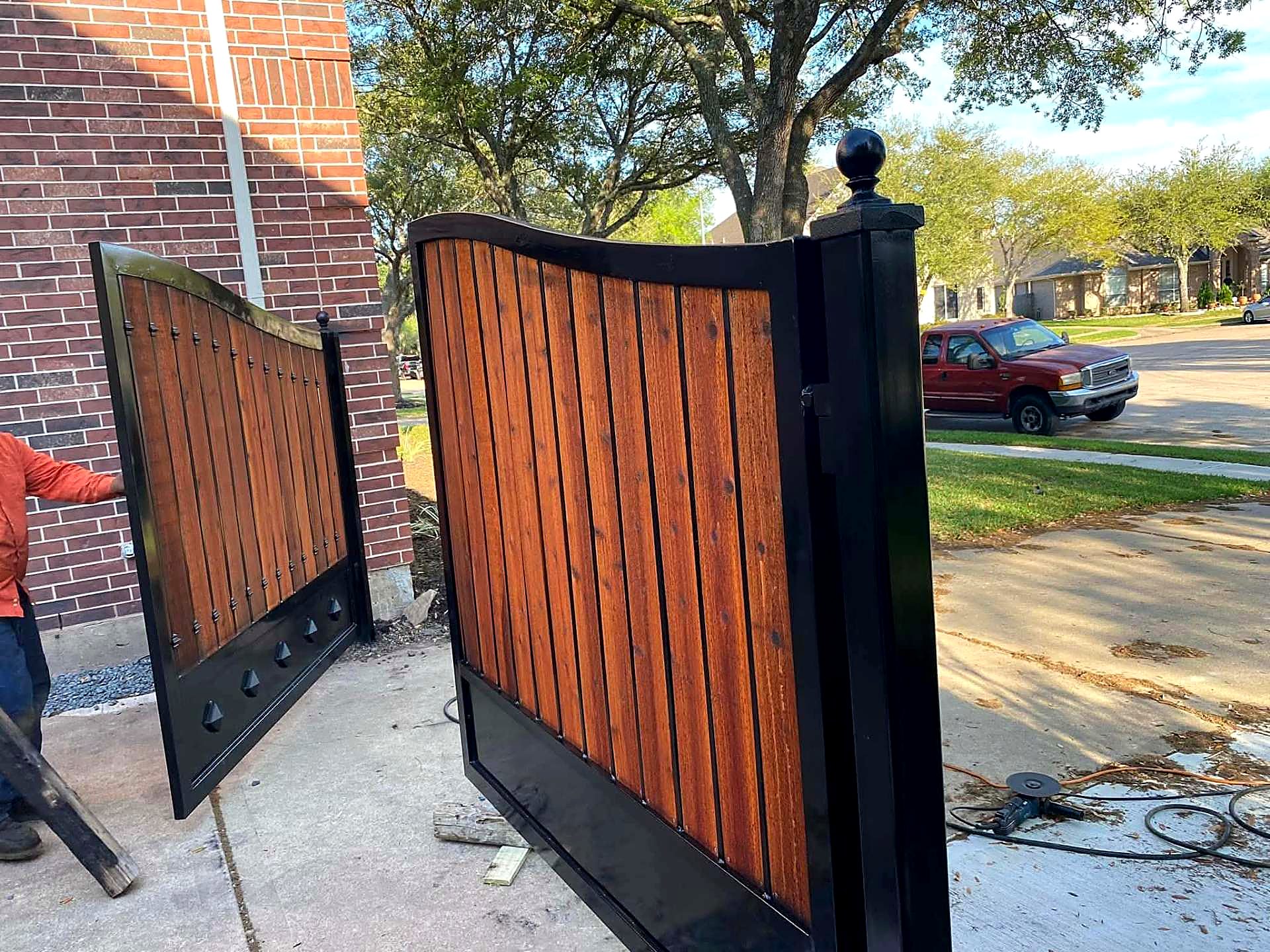 Two cedar-infill steel gate leaves being fitted at a driveway