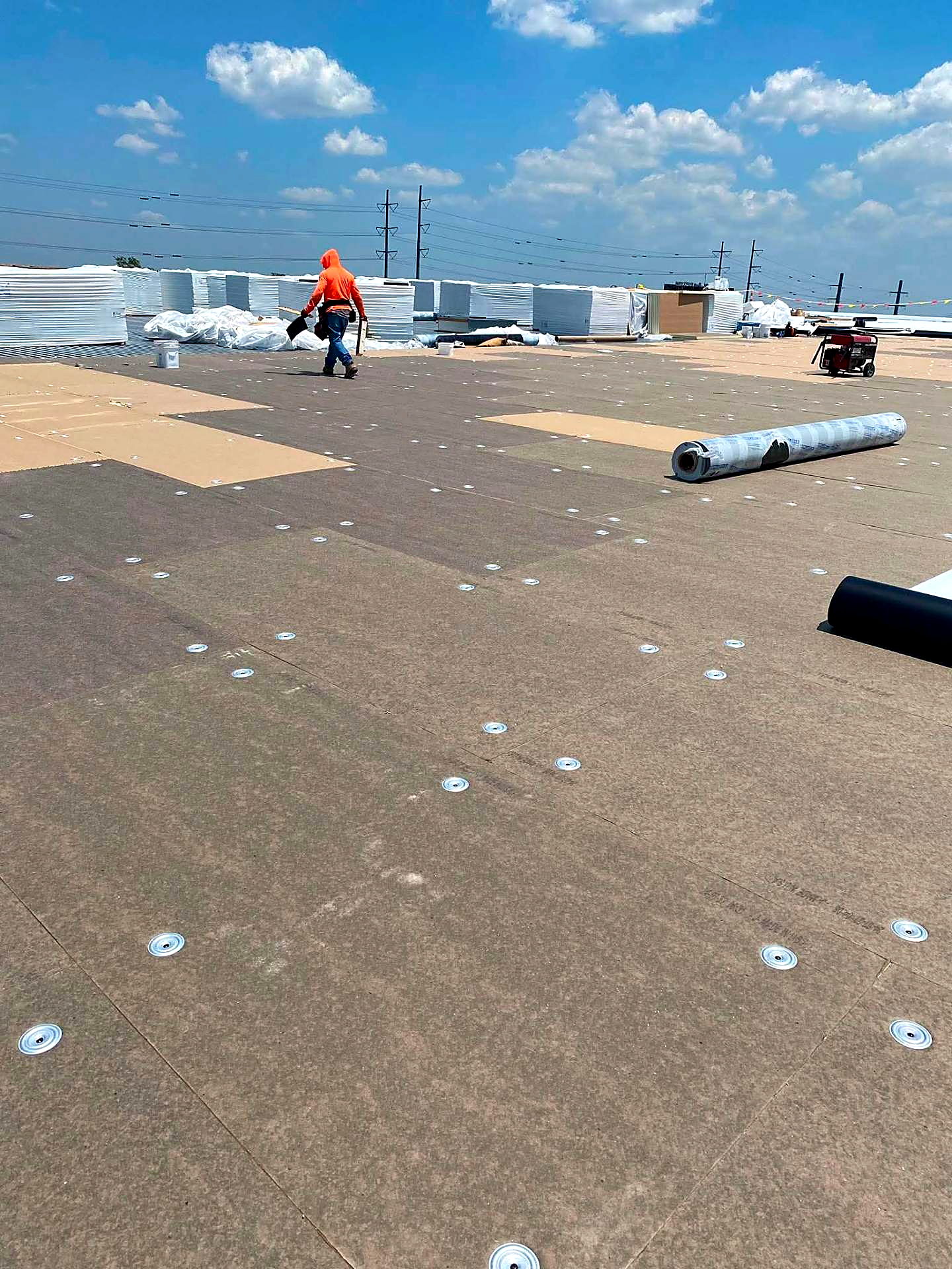 Base sheet fastened across a large commercial roof deck with insulation stacked behind