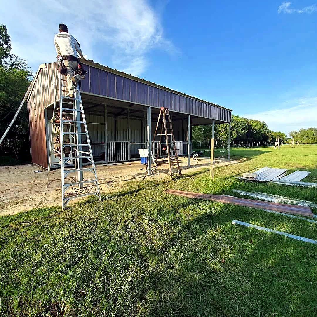 Loafing shed barn under construction with roof panels and stacked steel on the grass